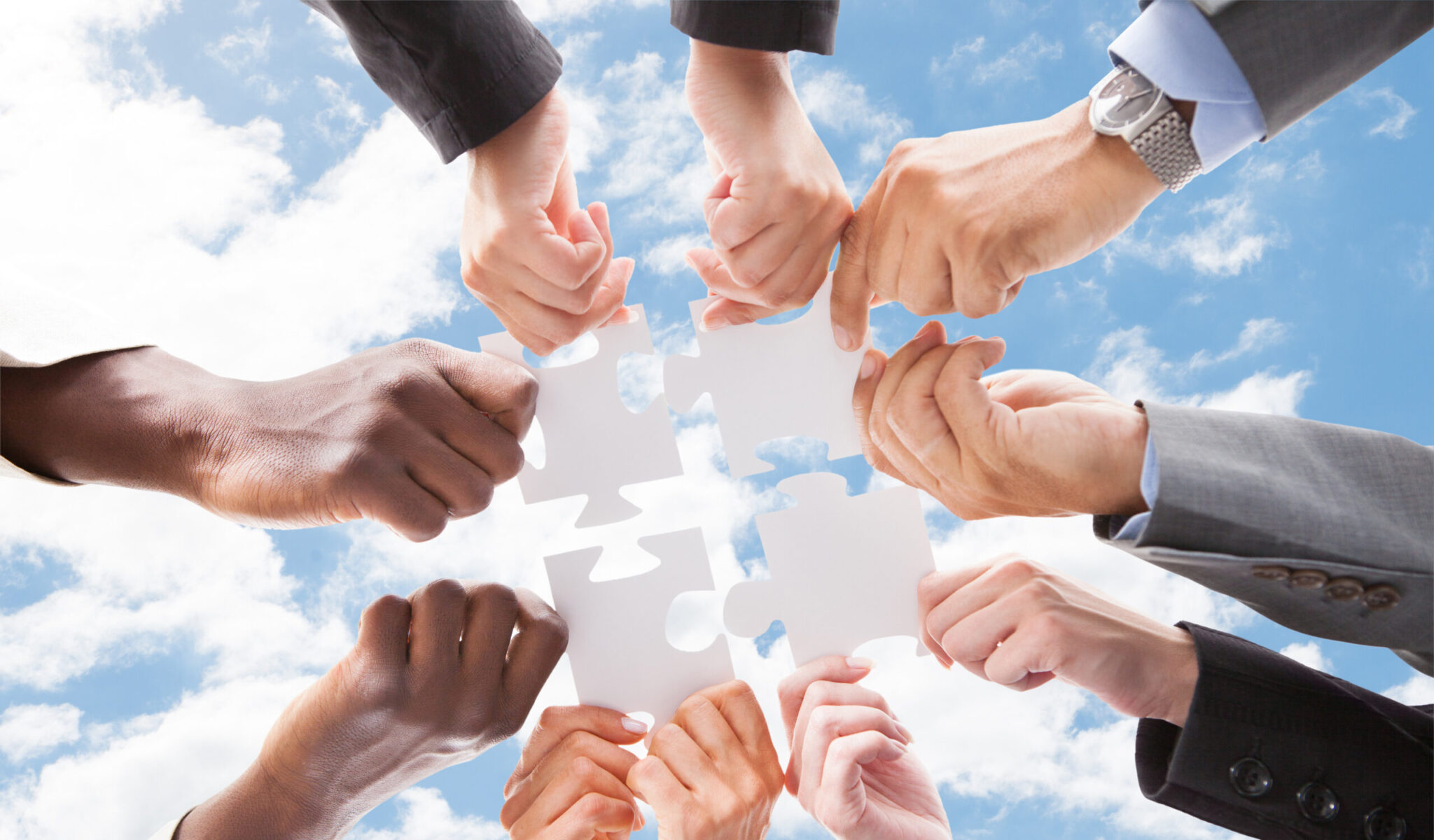 Directly below shot of multiethnic business people assembling jigsaw puzzle against sky